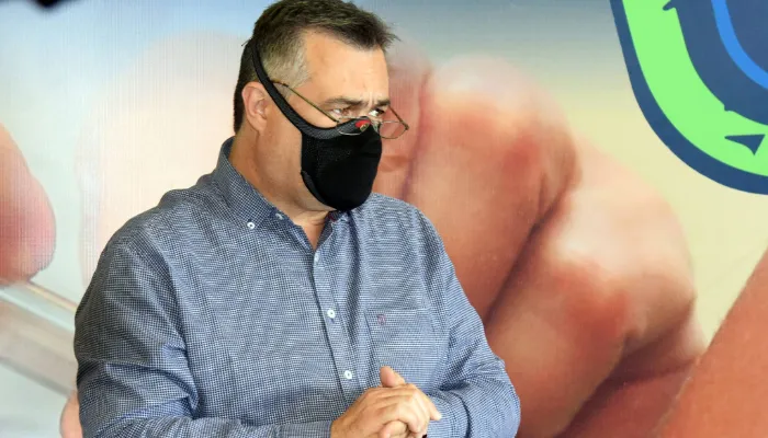 Na imagem, o secretário da Saúde do Paraná, Beto Preto, aparece usando máscara e óculos de grau enquanto presta entrevista em coletiva de imprensa.