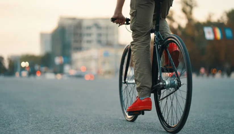 A foto mostra as pernas de um homem andando de bicicleta. Ele veste uma calça cargo e tênis vermelhos.