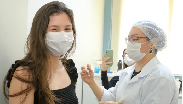 A foto mostra uma mulher recebendo uma dose da vacina contra o coronavírus. Quem aplica a dose é uma enfermeira.