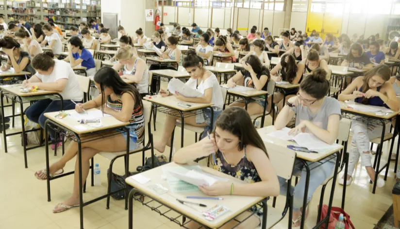 A foto mostra uma sala de aula com vestibulandos sentados em todas as carteiras fazendo a prova.