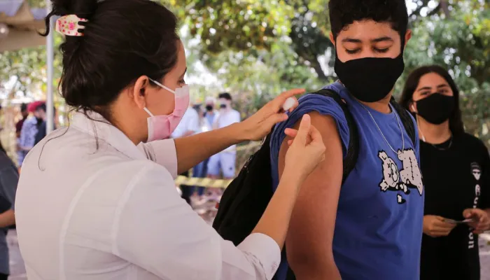 A foto mostra uma enfermeira aplicando uma dose de vacina no braço de um menino.
