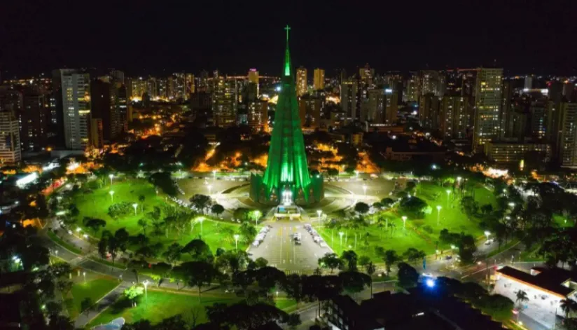 Foto aérea noturna de Maringá. Com foco na Catedral da cidade, que está iluminada com luzes verdes.