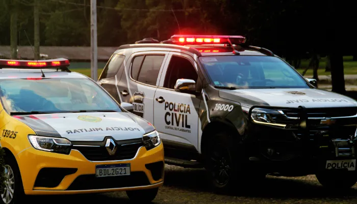A imagem mostra dois carros. Do lado esquerdo da foto, está um veículo da polícia militar e, do lado direito, está um veículo da polícia civil. As sirenes de ambos estão ligadas.