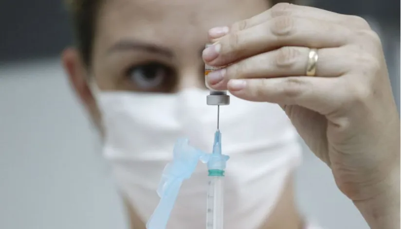 A foto mostra uma enfermeira segurando uma dose de vacina enquanto aspira o líquido com uma seringa