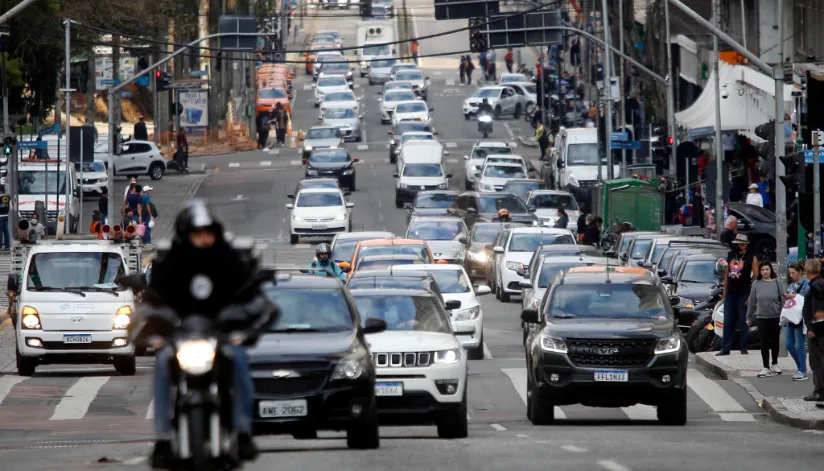 A foto mostra carro e motos no trânsito de uma cidade.
