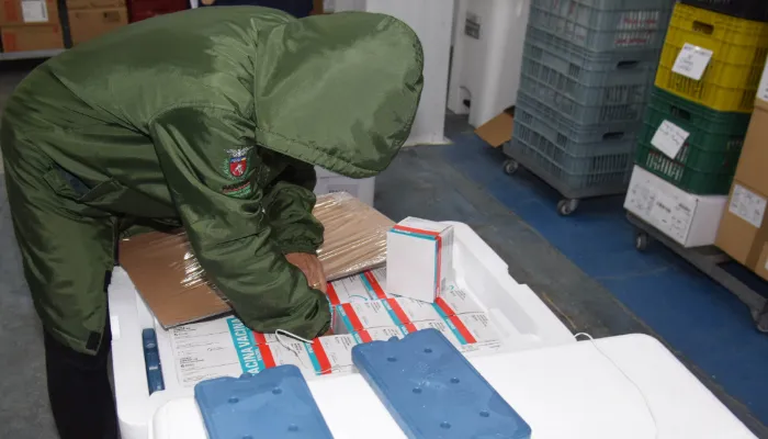A imagem mostra um funcionário do Governo, trajado em verde, retirando as caixas com os imunizantes de dentro dos isopores.